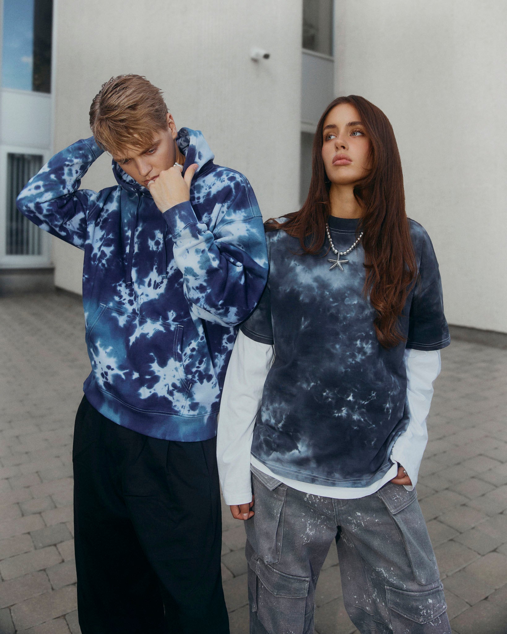 A navy blue and light blue tie-dye pullover hoodie with a drawstring hood and kangaroo pocket, displayed against a solid off-white background.