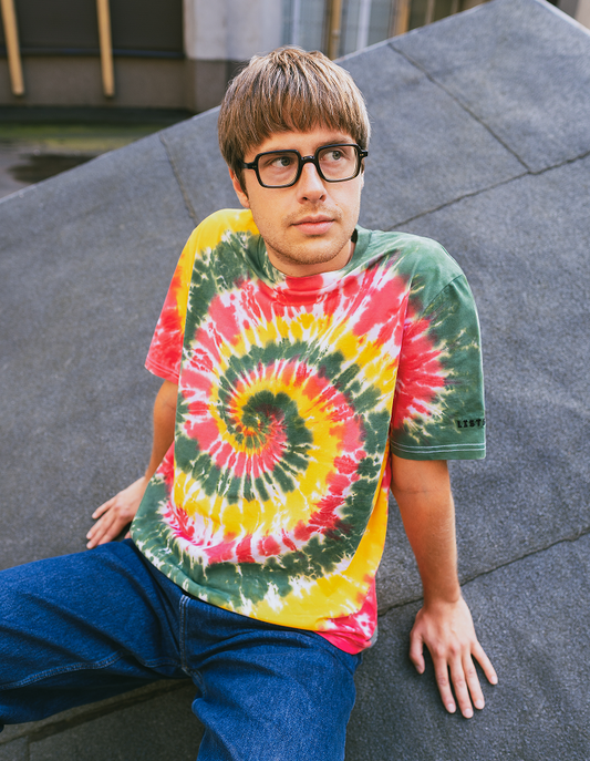 Person wearing a tie-dye t-shirt sitting on a concrete surface
