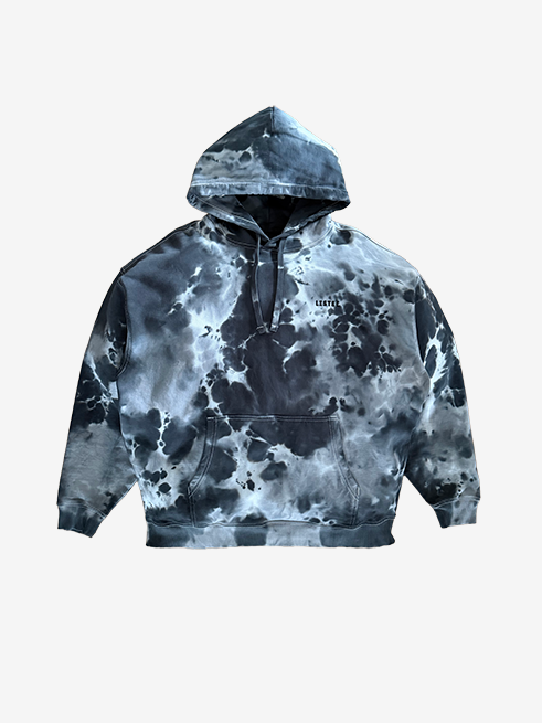 A black and grey tie-dye pullover hoodie with a small black text logo on the left chest, displayed against a solid light gray background.