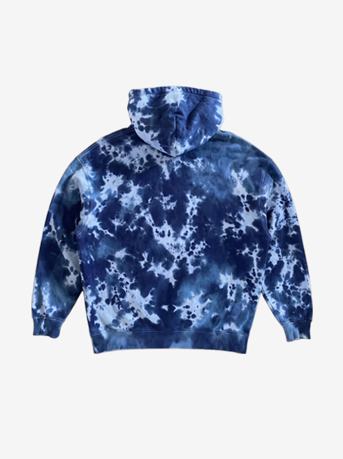 A navy blue and light blue tie-dye hoodie shown from the back, featuring a classic indigo and white marbled pattern, photographed against a solid off-white background.